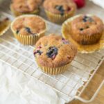 Fresh blueberry muffins cooling on a wire rack, showcasing golden-brown tops, blueberries inside, and a delightful homemade baked goods appearance perfect for breakfast or snack.