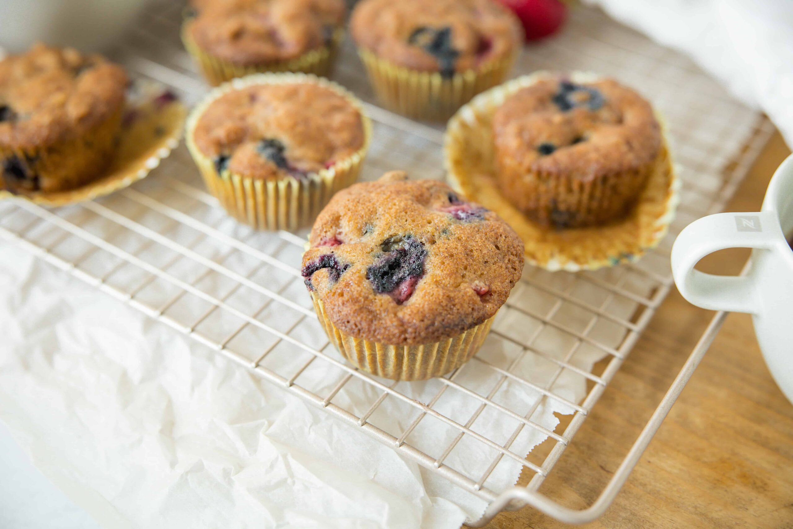 Fresh blueberry muffins cooling on a wire rack, showcasing golden-brown tops, blueberries inside, and a delightful homemade baked goods appearance perfect for breakfast or snack.