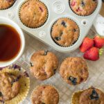 Freshly baked blueberry muffins with strawberries on a cooling rack, accompanied by a cup of tea, showcasing delicious homemade baked goods perfect for breakfast or snack.