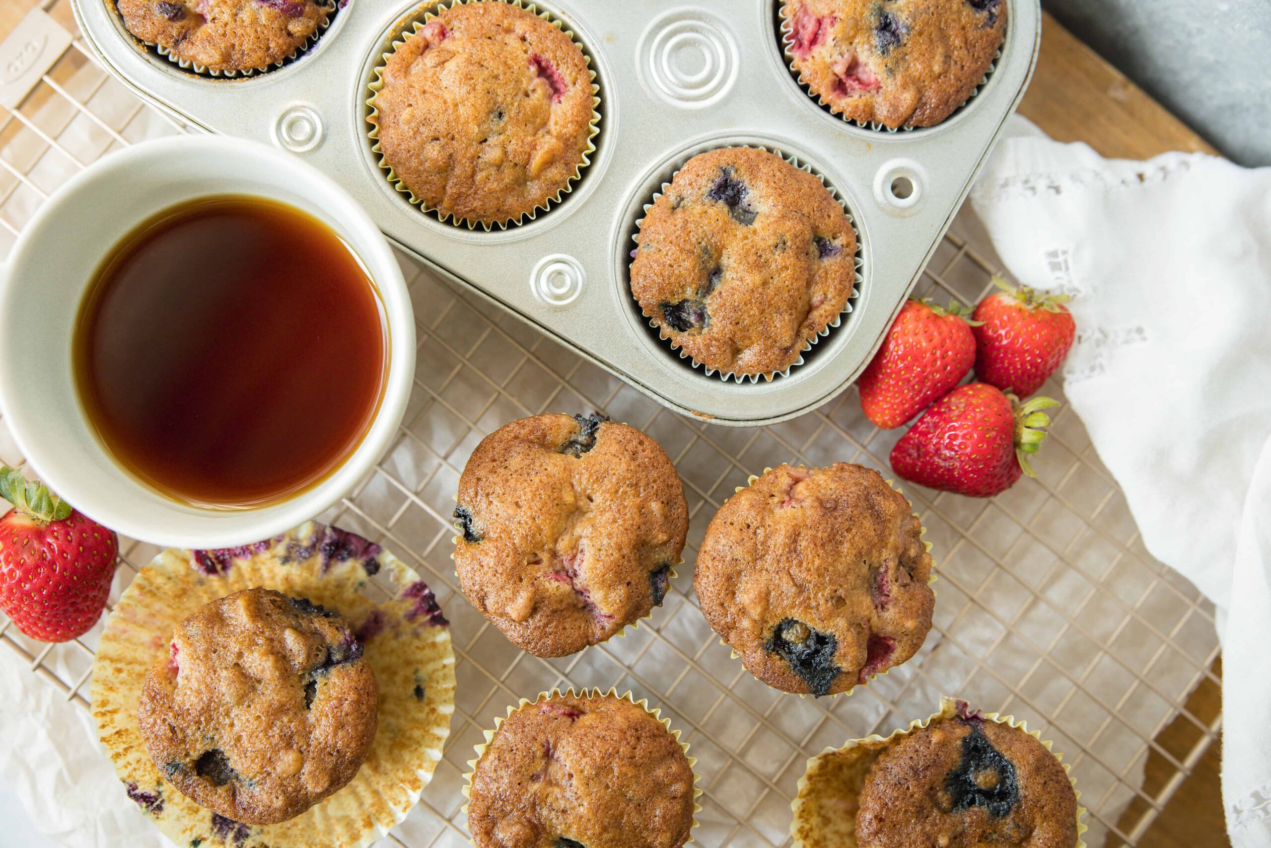 Freshly baked blueberry muffins with strawberries on a cooling rack, accompanied by a cup of tea, showcasing delicious homemade baked goods perfect for breakfast or snack.