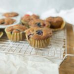 Fresh homemade blueberry muffins on a cooling rack with a cup of coffee in the background, perfect for breakfast or snack.