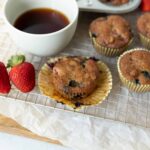 Fresh homemade blueberry muffins with strawberries and a cup of black coffee, served on a wire cooling rack for breakfast or snack. Perfect for berry lovers and baking enthusiasts.