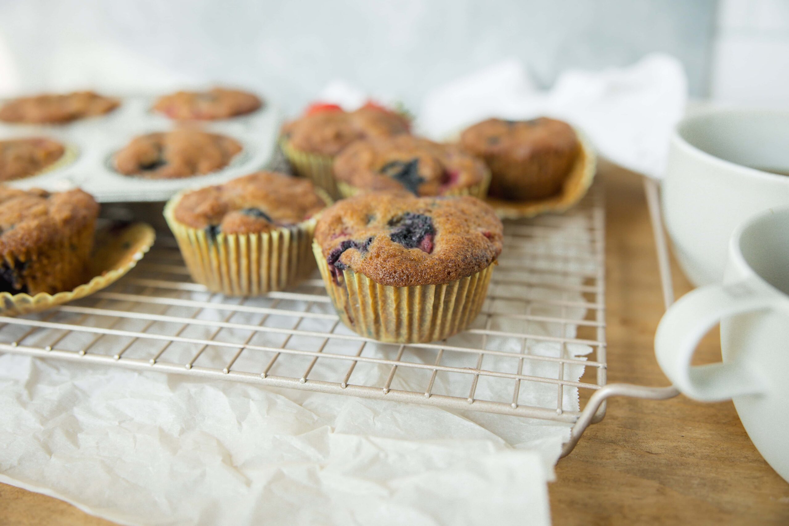 Fresh homemade blueberry muffins on a cooling rack with a cup of coffee in the background, perfect for breakfast or snack.