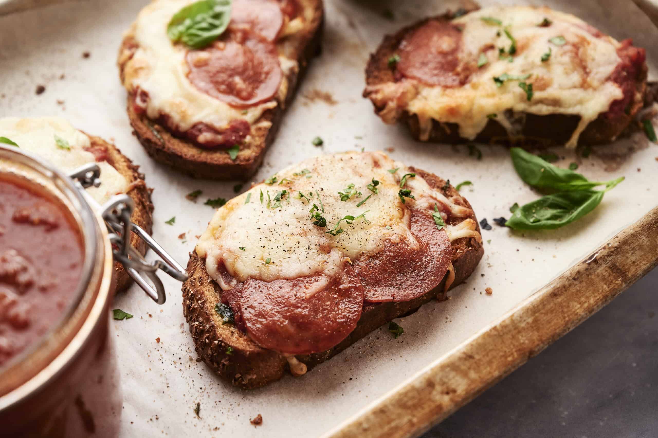 Savory mini pepperoni and cheese pizza bread slices topped with melted cheese and fresh herbs, served on a rustic wooden board. Perfect for snack or appetizer recipes, featuring easy-to-make pizza bread ideas.