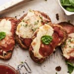 Oven-baked pepperoni and cheese mini pizzas on rustic bread slices with fresh basil garnish, served on parchment paper with a side of tomato sauce and a bowl of fresh spinach leaves, perfect for homemade pizza night.