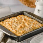 Baked crumb-topped casserole dish on a rustic kitchen table, ready to serve, with a white plate and decorative jar in the background, showcasing comforting homemade comfort food.