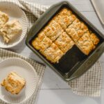 Butterscotch Lemon Bars, baked to golden perfection, served on white plates with a checkered cloth, showcasing their flaky crust and tart lemon filling, perfect for dessert or afternoon tea.