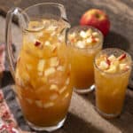 Refreshing apple juice pitcher and glasses with chopped apples and ice cubes on rustic wooden table, perfect for healthy fruit drink recipes.