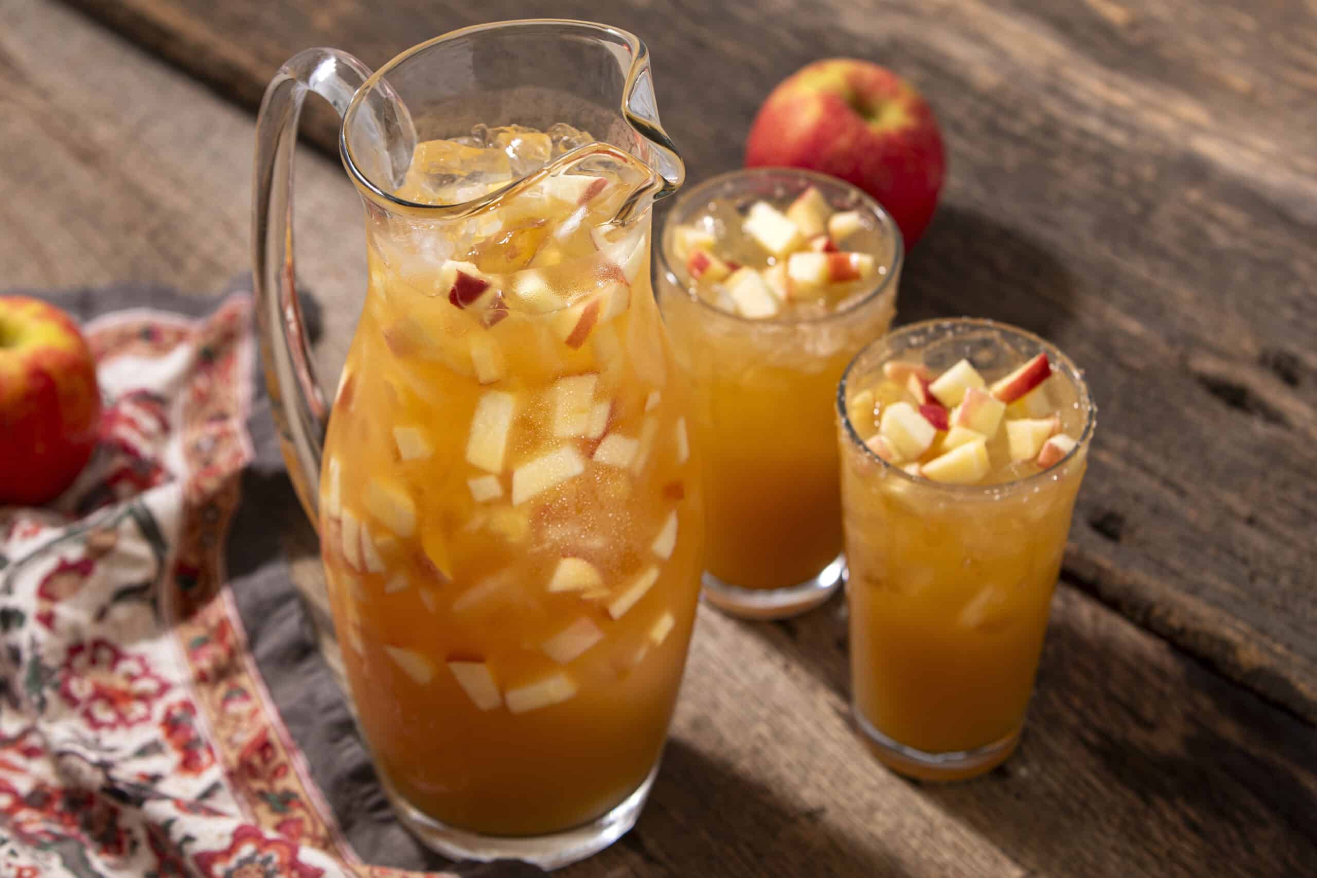Refreshing apple juice pitcher and glasses with chopped apples and ice cubes on rustic wooden table, perfect for healthy fruit drink recipes.