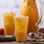 Fresh apple juice served in tall glasses with ice, with a pitcher of homemade apple cider in the background. Perfect for refreshing summer drinks and healthy beverage options.