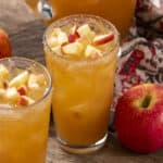 Fresh apple juice with chopped apples on top in tall glasses, surrounded by whole apples and a rustic wooden table for a healthy fruit drink presentation.