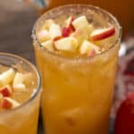 Fresh apple juice with chopped apple pieces on top, served in tall glasses for a refreshing beverage.