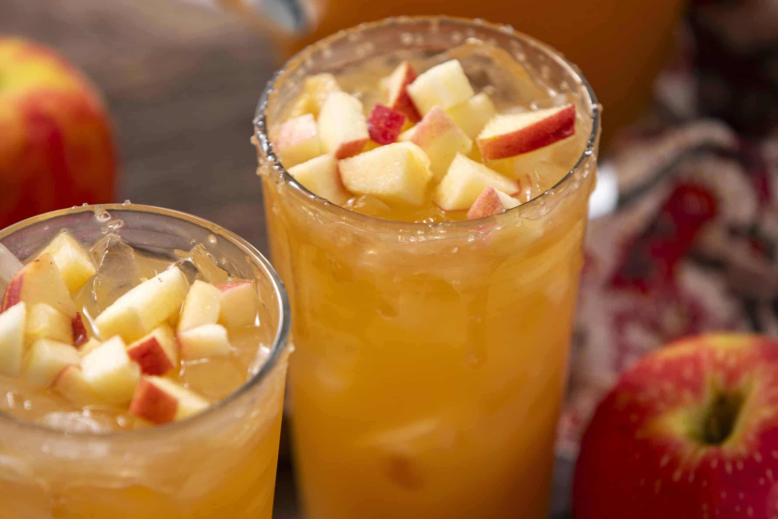 Fresh apple juice with chopped apple pieces on top, served in tall glasses for a refreshing beverage.