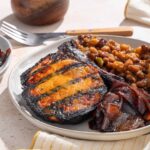 Baked fish fillet with tomato sauce served with baked beans and caramelized onions on a white ceramic plate.