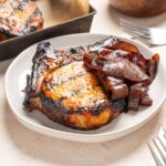 Juicy grilled steak topped with melted cheese served with caramelized onions on a white plate. Perfect for a hearty dinner, complemented by tender, flavorful roasted vegetables and a rustic meal presentation.