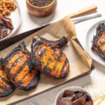 Grilled salmon steaks with charred exterior served on a baking sheet with grilled onions and various side dishes.