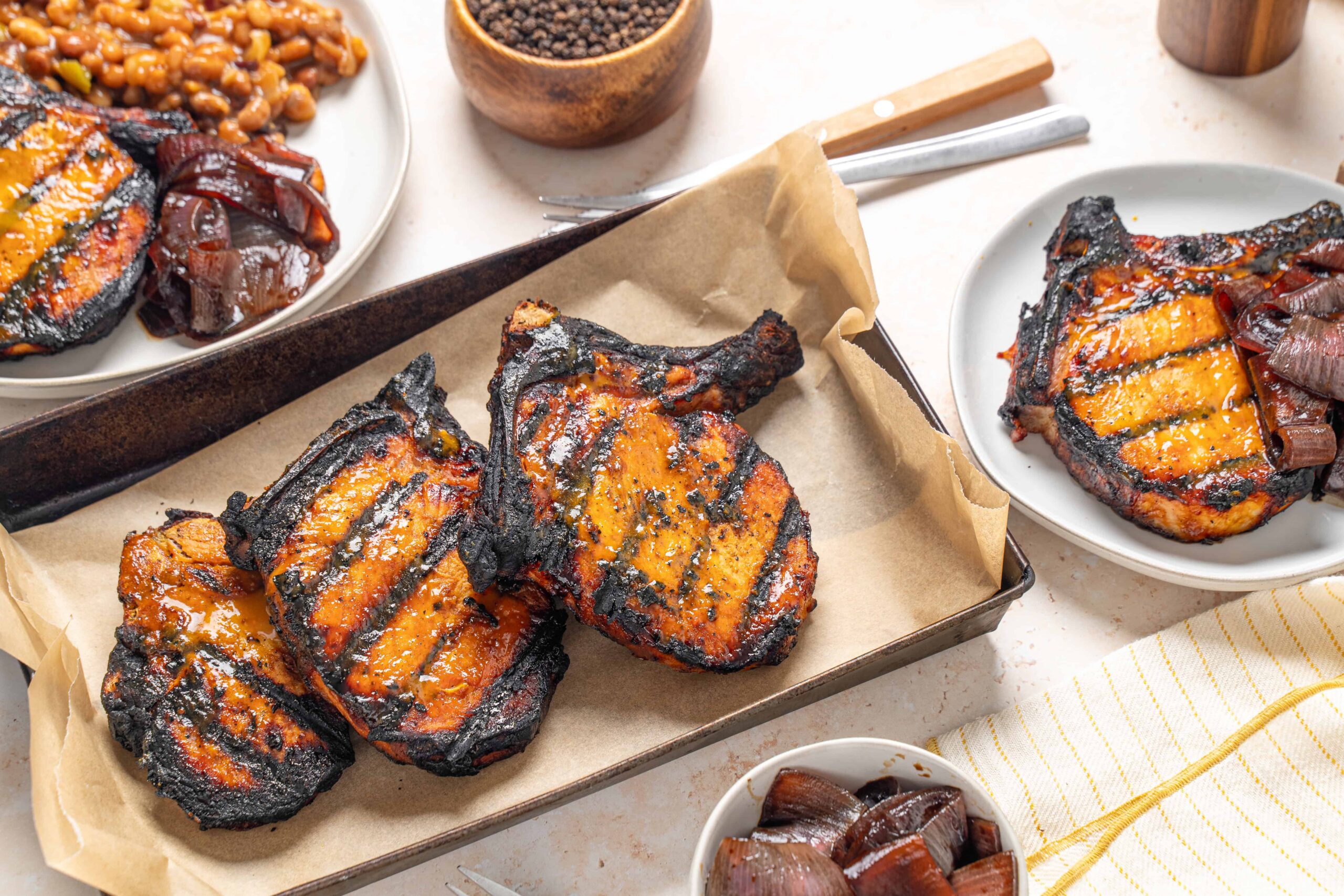 Grilled salmon steaks with charred exterior served on a baking sheet with grilled onions and various side dishes.