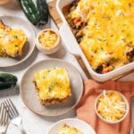 Creamy Tex-Mex casserole topped with melted cheese, served with shredded cheese and fresh vegetables, perfect for a comforting family meal or dinner.