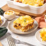 Creamy Mexican beef casserole with melted cheese, seasoned ground beef, and a crispy topping served with fresh jalapeño peppers and shredded cheese on a rustic table.