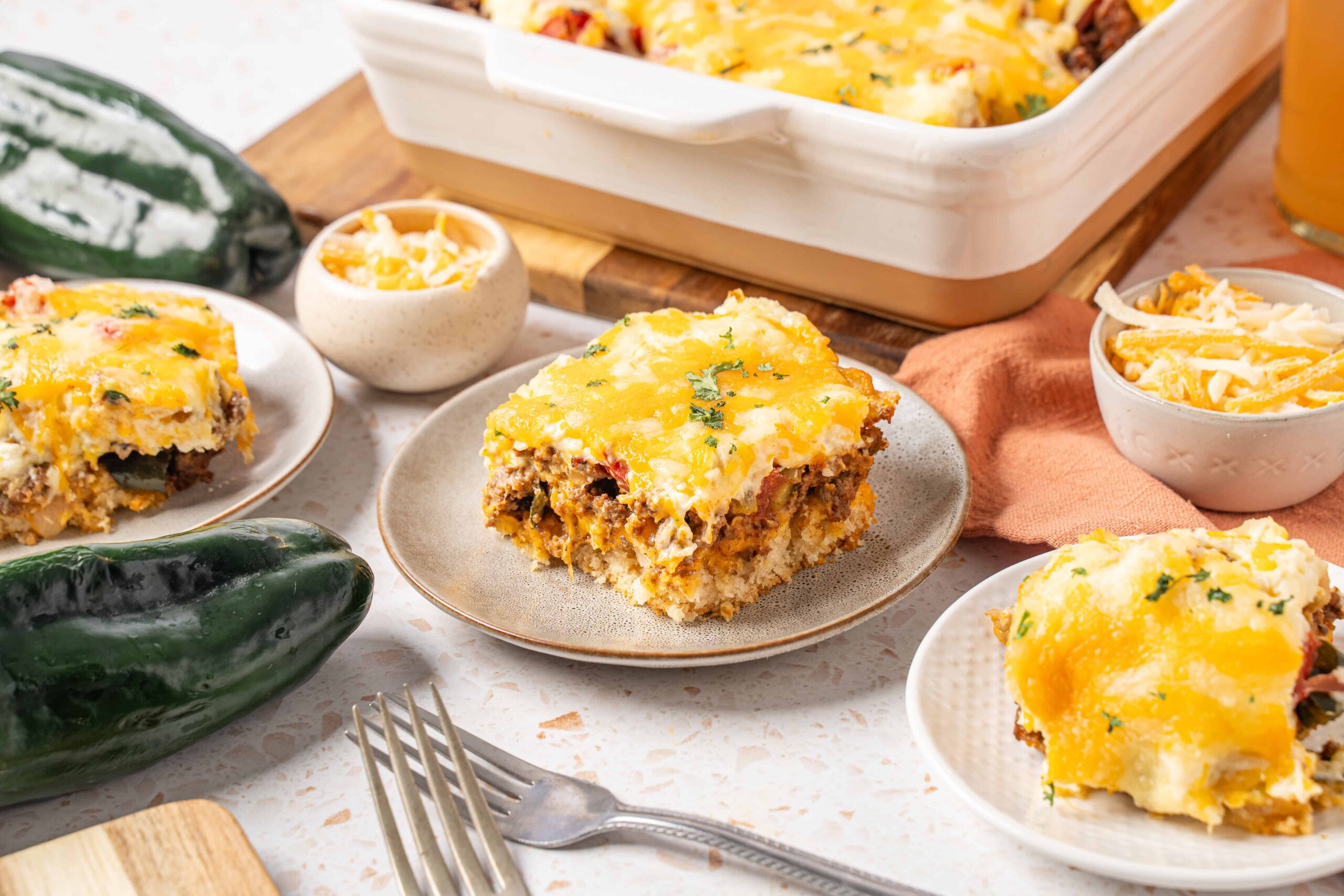 Creamy Mexican beef casserole with melted cheese, seasoned ground beef, and a crispy topping served with fresh jalapeño peppers and shredded cheese on a rustic table.