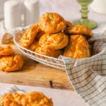 Fried cheese fritters served on a wire basket with a checkered cloth, fresh and crispy, perfect for appetizer or snack, with a rustic wooden cutting board background.