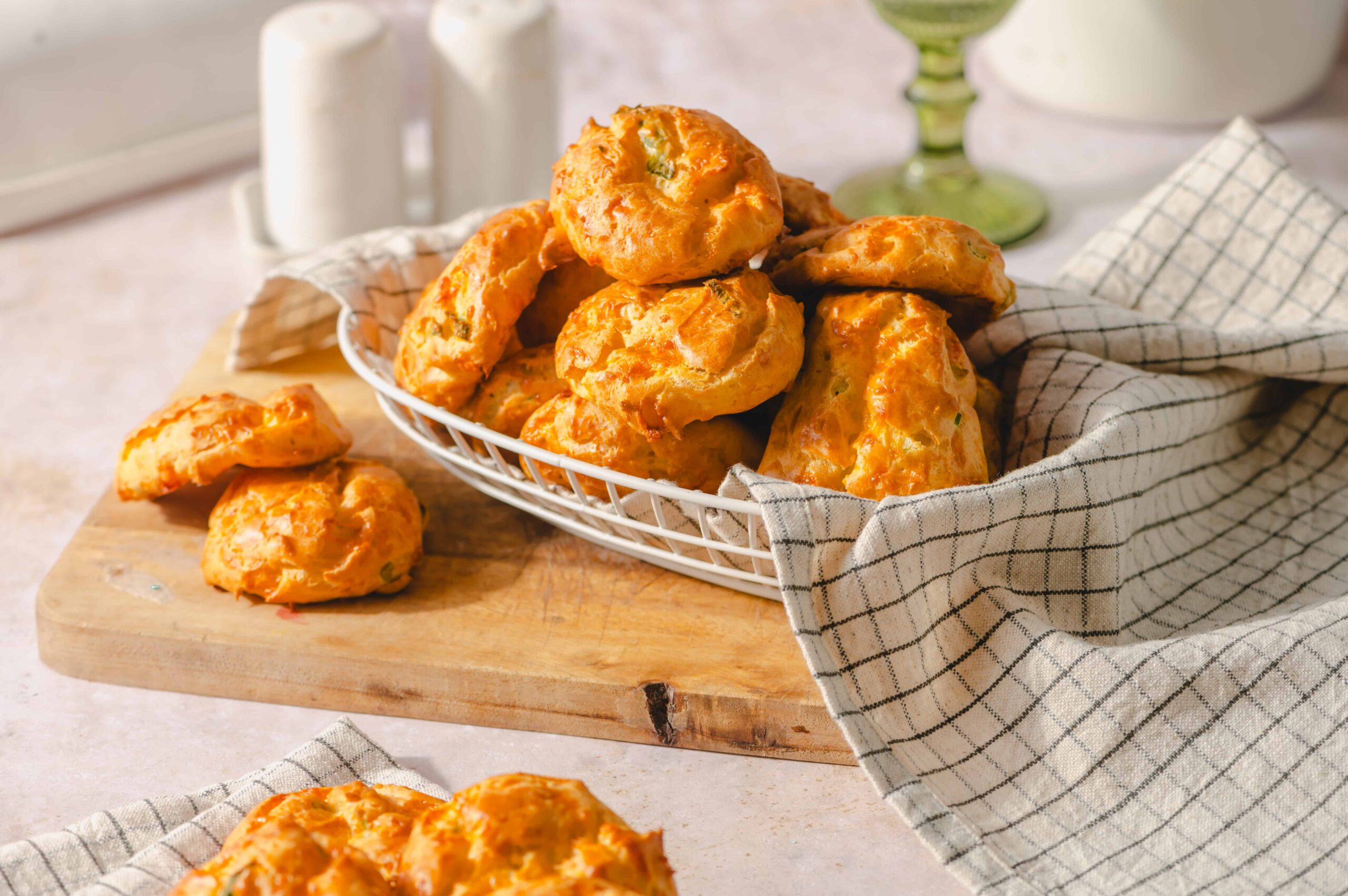 Fried cheese fritters served on a wire basket with a checkered cloth, fresh and crispy, perfect for appetizer or snack, with a rustic wooden cutting board background.