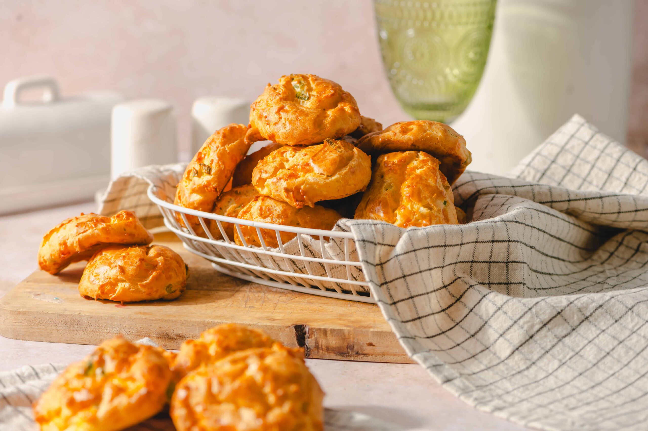 Fried cheese biscuits stacked in a basket with a checkered cloth, served on a wooden tray with a glass of water in the background, perfect for an appetizer or snack.