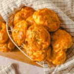 Soft cheddar cheese biscuits on a wire basket with a checkered cloth, perfect for breakfast or snack, golden baked, flaky, and flavorful.