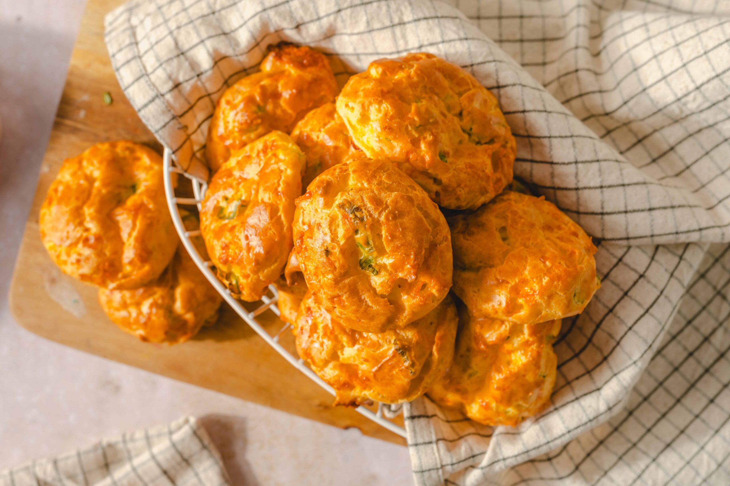 Soft cheddar cheese biscuits on a wire basket with a checkered cloth, perfect for breakfast or snack, golden baked, flaky, and flavorful.