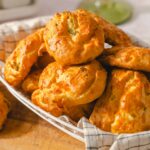 Golden cheesy crab cakes served hot on a woven basket with a checkered cloth, perfect for appetizers or snacks.