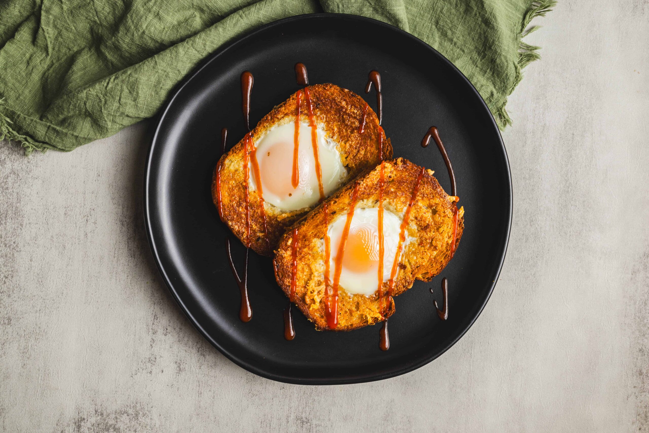Fried egg in bread, topped with ketchup and served on a black plate, with a green napkin, perfect for breakfast or brunch.