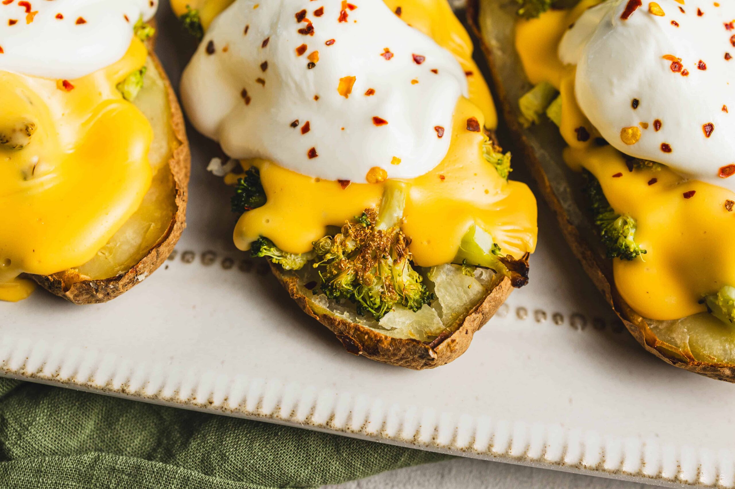 Roasted sweet potato boats topped with cheesy broccoli, sour cream, and chili flakes, served on a white platter.