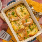 Scrambled eggs with sliced bread topped with chopped green onions, grated cheese, and herbs in a white baking dish, ready to serve for breakfast or brunch.