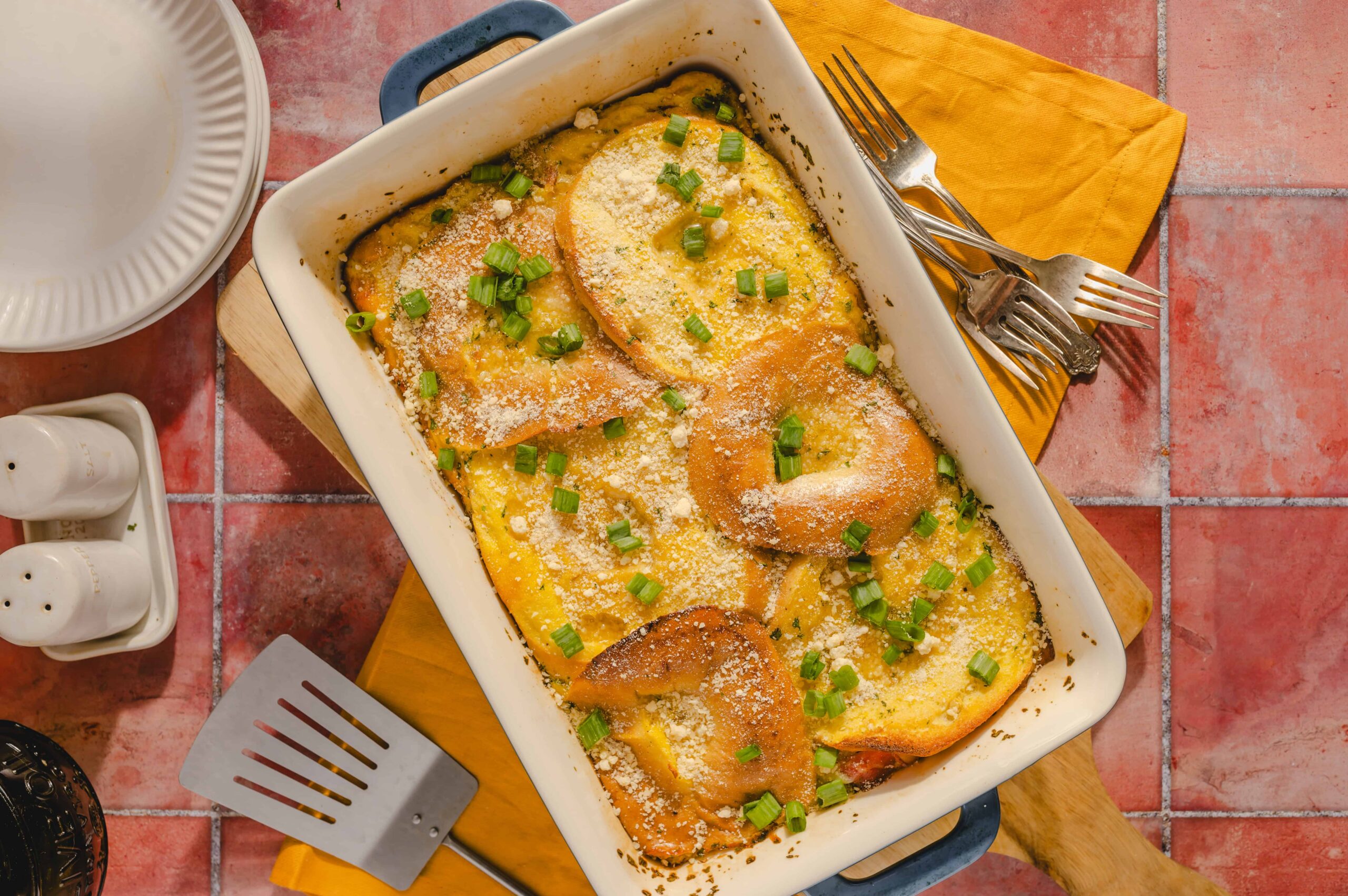 Scrambled eggs with sliced bread topped with chopped green onions, grated cheese, and herbs in a white baking dish, ready to serve for breakfast or brunch.