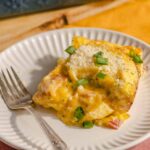 Cheesy baked breakfast casserole with eggs, ham, and green onions served on a white plate. Perfect for brunch or family gatherings, easy to prepare and full of flavor.