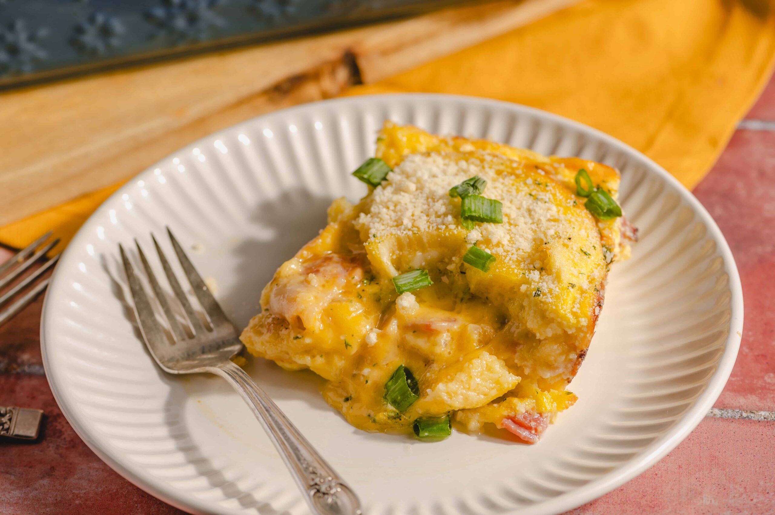 Cheesy baked breakfast casserole with eggs, ham, and green onions served on a white plate. Perfect for brunch or family gatherings, easy to prepare and full of flavor.