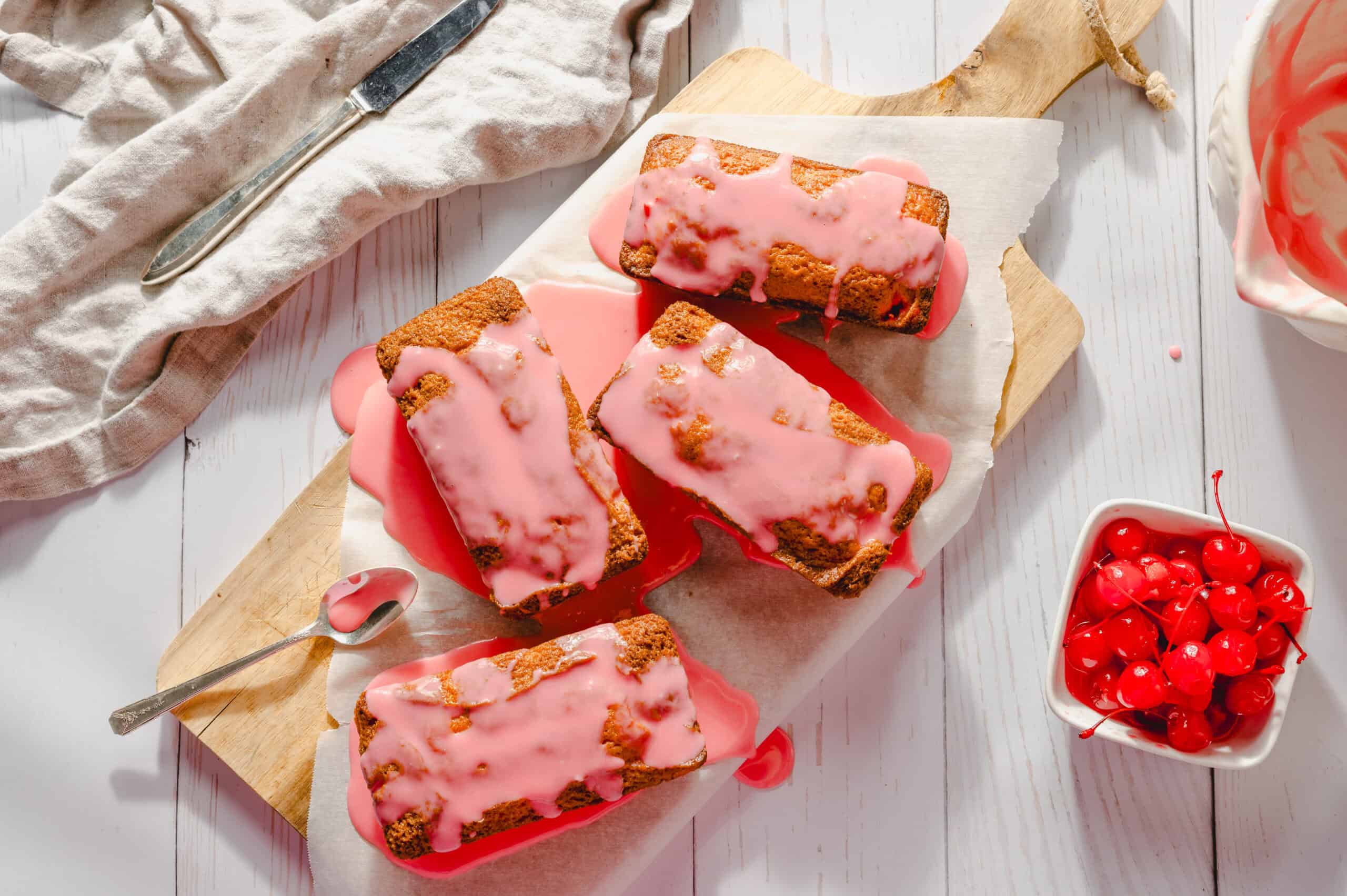 Sweet cherry loaf cakes with pink glaze on wooden cutting board, fresh cherries in white bowl, spring dessert, and homemade baking, perfect for spring desserts and cherry recipes.