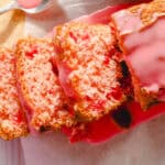 Moist strawberry cake with pink icing glaze on a wooden board with a piece cut out, showcasing the fluffy inside and fresh strawberry flavor, perfect for desserts and snack recipes.