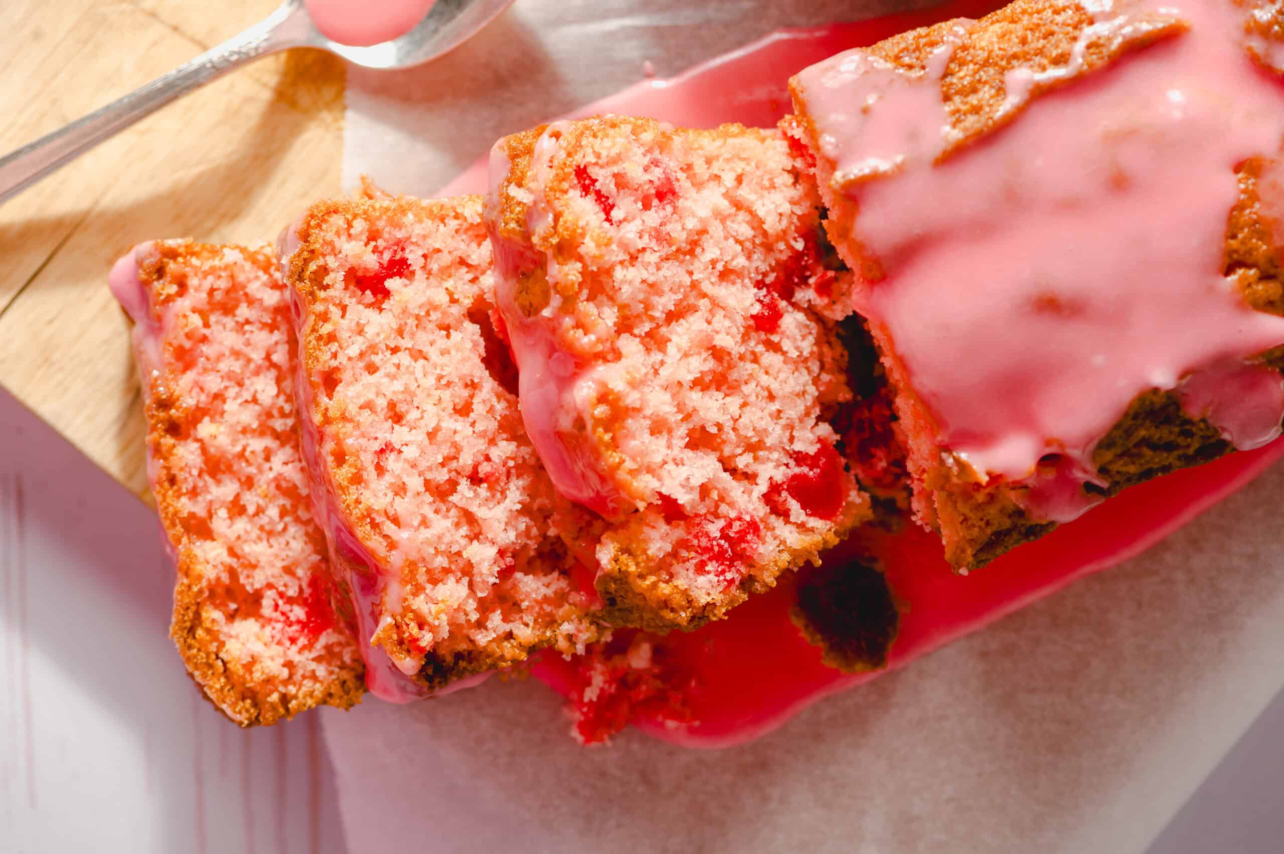 Moist strawberry cake with pink icing glaze on a wooden board with a piece cut out, showcasing the fluffy inside and fresh strawberry flavor, perfect for desserts and snack recipes.