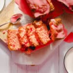 Moist, tender strawberry cake slices with pink glaze drizzled on top, served on parchment paper with a side of milk, presented on a rustic wooden surface for a delicious dessert dessert.