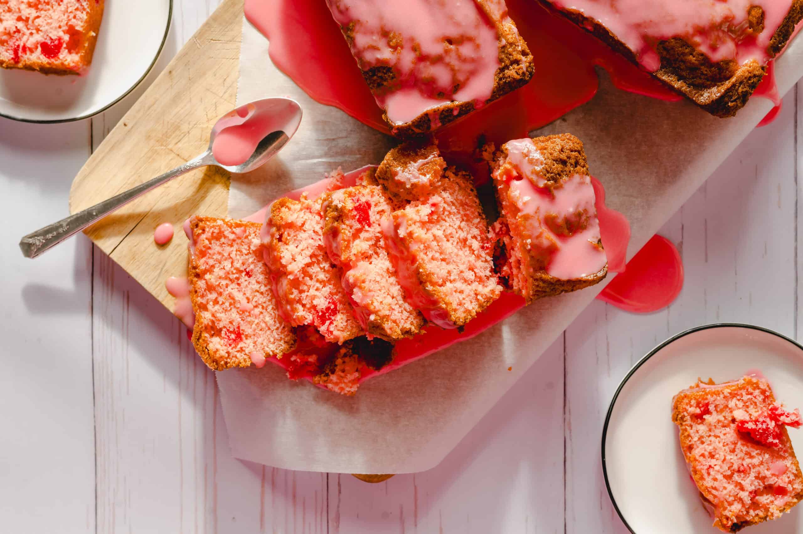 Moist, tender strawberry cake slices with pink glaze drizzled on top, served on parchment paper with a side of milk, presented on a rustic wooden surface for a delicious dessert dessert.