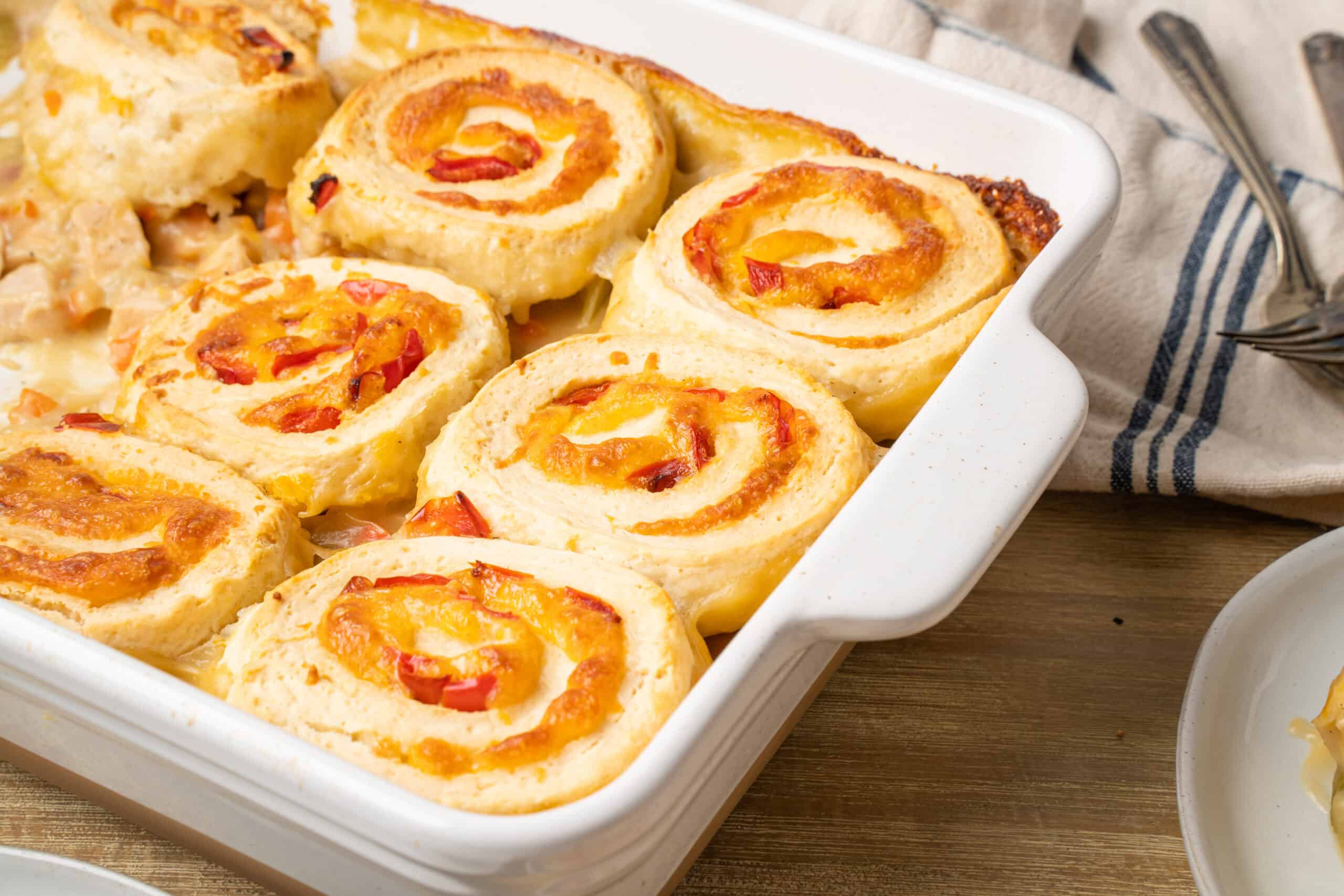 Savory cheesy chicken and vegetable pinwheel casserole baked in a white dish with melted cheese and colorful peppers. Perfect for family dinners or gatherings.