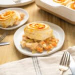 Creamy chicken and vegetable pot pie with flaky biscuit topping, served on a white plate with a rustic wooden table background. Perfect comfort food recipe featuring tender chicken, carrots, celery, and savory gravy.