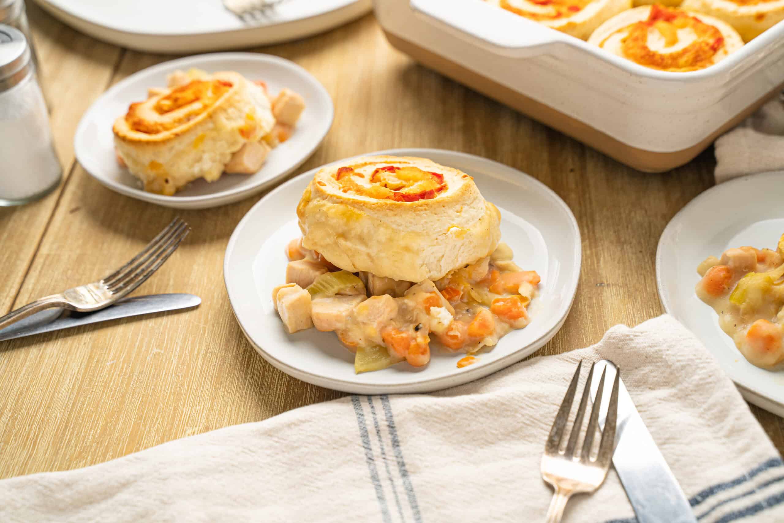 Creamy chicken and vegetable pot pie with flaky biscuit topping, served on a white plate with a rustic wooden table background. Perfect comfort food recipe featuring tender chicken, carrots, celery, and savory gravy.