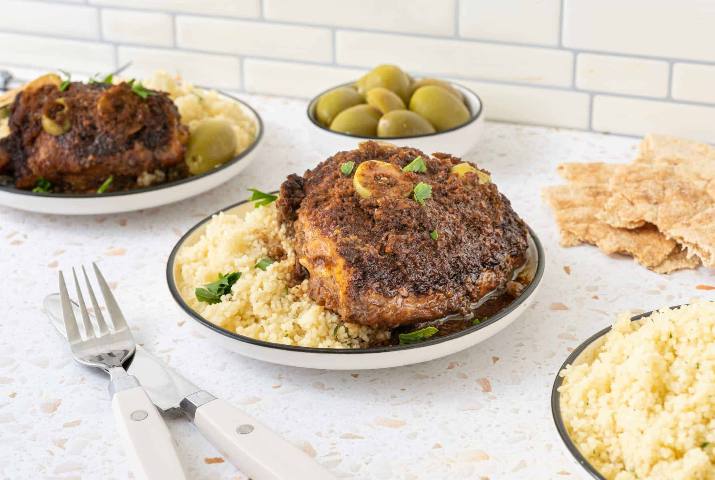 Succulent Moroccan chicken tagine served with fluffy couscous, green olives, and crispy flatbread on a marble countertop. Authentic North African cuisine with rich spices and tender meat.