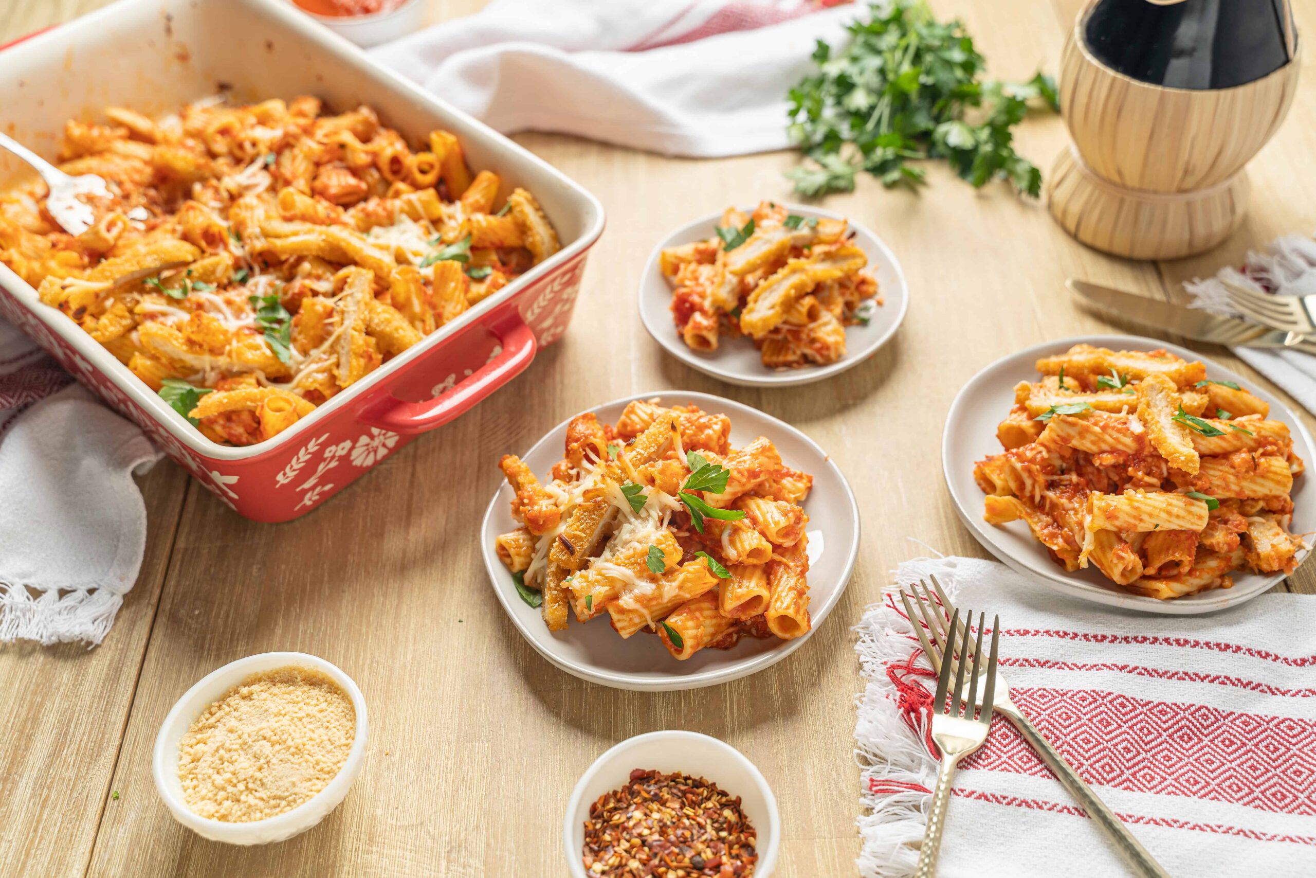 Creamy baked pasta casserole with tomato sauce, cheese, and herbs served in white plates, featuring Italian comfort food ideal for family dinners and gatherings.