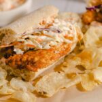 Juicy fried chicken sandwich with coleslaw on a soft bun, served with potato chips, close-up, delicious comfort food, perfect for lunch or casual dining.