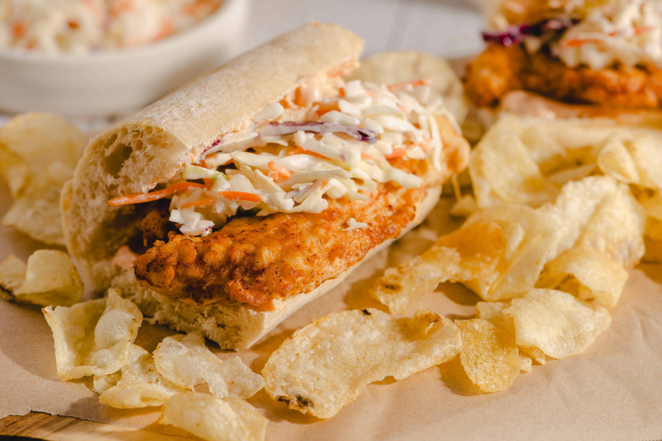 Juicy fried chicken sandwich with coleslaw on a soft bun, served with potato chips, close-up, delicious comfort food, perfect for lunch or casual dining.