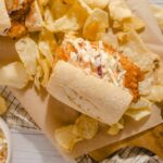 Fresh taco with shredded coleslaw and spicy meat filling, served with potato chips on a wooden cutting board, with a side of coleslaw in a small bowl, showcasing a delicious Mexican-inspired dish.