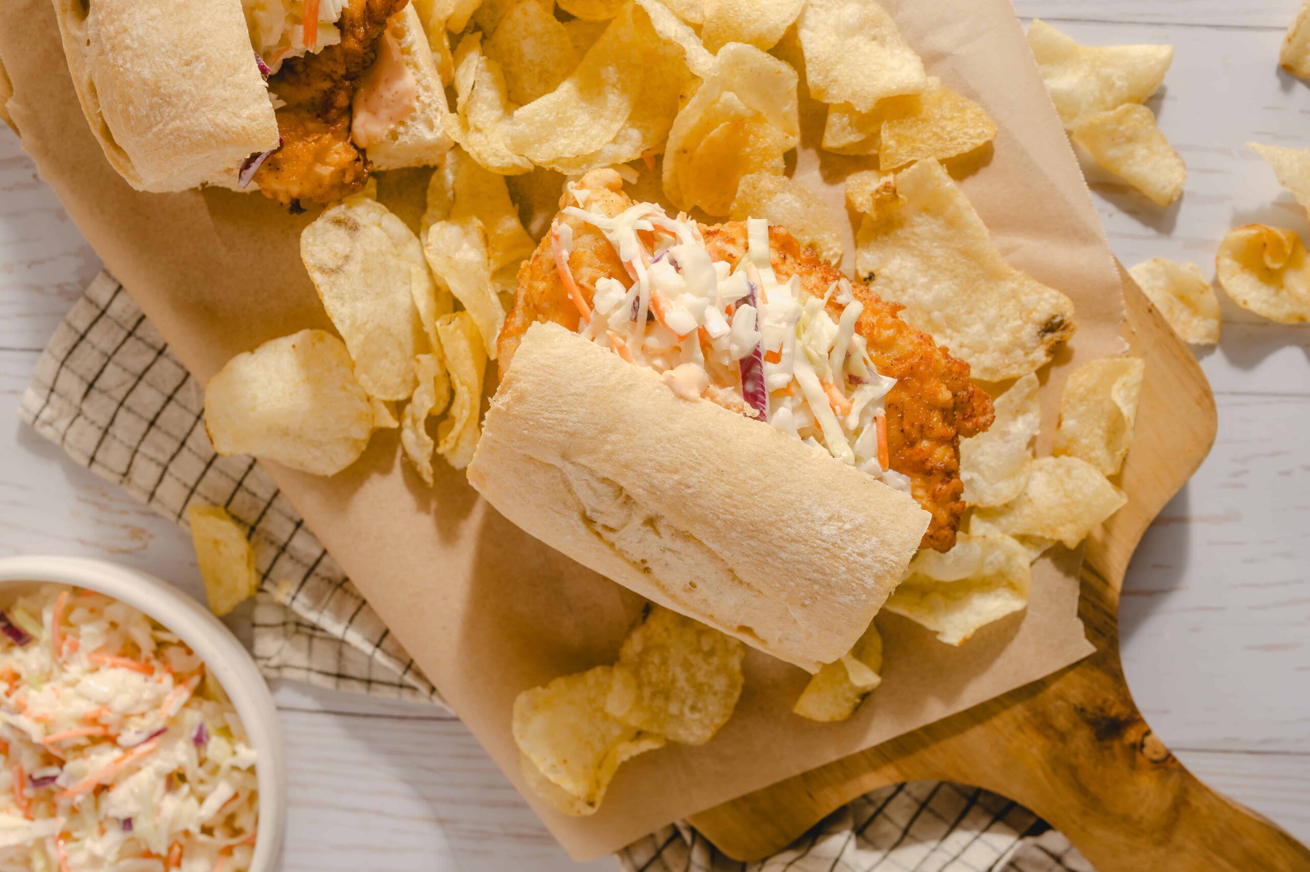 Fresh taco with shredded coleslaw and spicy meat filling, served with potato chips on a wooden cutting board, with a side of coleslaw in a small bowl, showcasing a delicious Mexican-inspired dish.